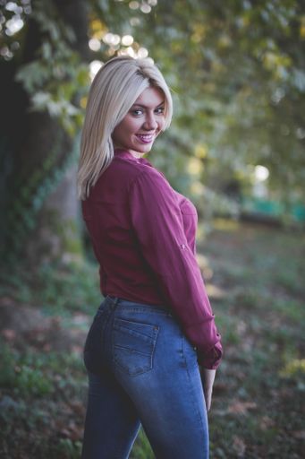 A vertical shot of young blonde female with pink lipstick and a pink blouse posing in a park