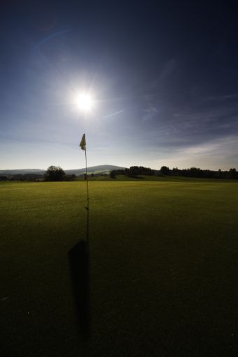 A beautiful scenery of a golf hole and a flag in a field against a bright sunny day background