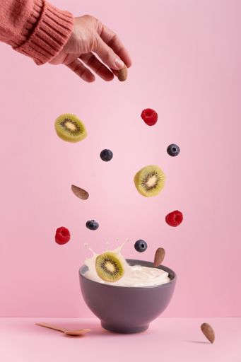 A vertical shot of different fruits and berries falling into a bowl of milk on a pink background