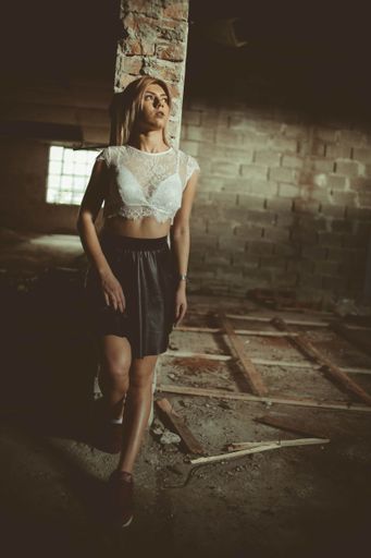 A vertical shot of a young blonde female posing leaning on a column inside an abandoned building
