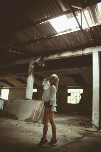 A vertical shot of a sexy blonde haired woman standing in the middle of the ruined room