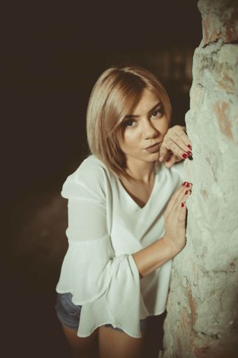 A vertical shot of a young blonde female leaning on the ruined wall of an abandoned building