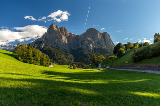 A field surrounded by rocks covered in greenery under a blue sky and sunlight in Italy