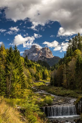 A vertical picture of a river in a forest with rocks under a cloudy sky on the background in Italy