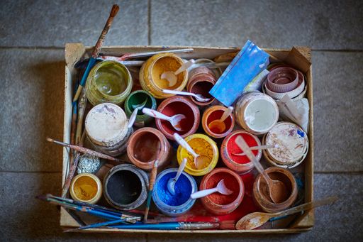 A box full of a lot of colorful paint pigments and brushes on a concrete surface