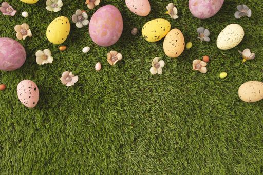 An overhead shot of colorful Easter eggs and flowers on a grassy lawn with space for your text