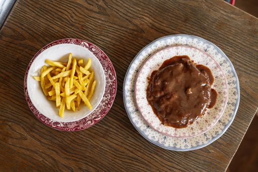 An overhead shot of a patty covered with thick savory sauce and a bowl of crispy French fries