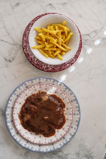 An overhead shot of a patty covered with thick savory sauce and a bowl of crispy French fries