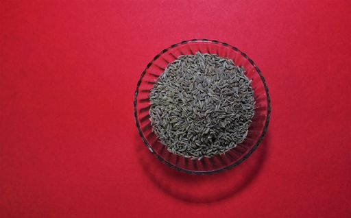 A bowl of caraway seeds on a red background