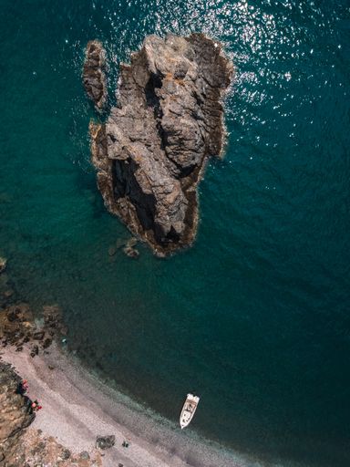 A top view shot of tropical waters, a hill island, and a white boat close to the shore