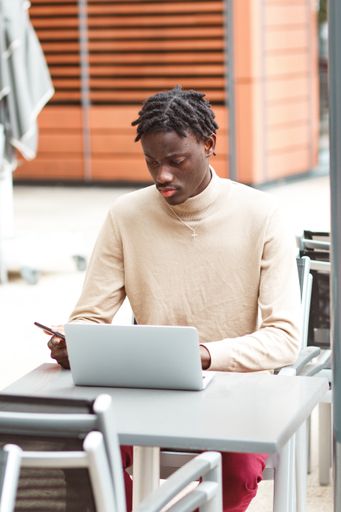 A vertical shot of a young Afro-American entrepreneur working on his laptop using his phone