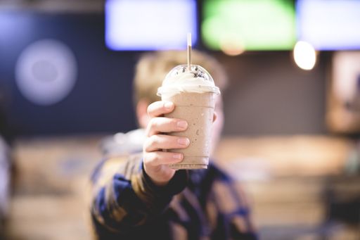 A man holding a tasty frappe in a plastic take away cup with blurred background