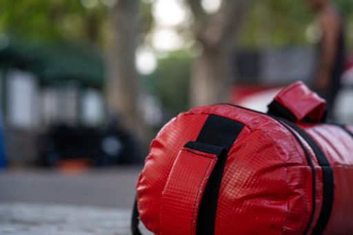 A closeup of a red punching bag on the ground in a park with a blurry background