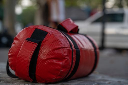 A closeup of a red punching bag on the ground in a park with a blurry background