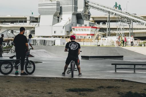 a male sitting on a bicycle in a skate park with building in the background