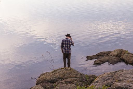 A male standing on a rock near a sea looking down