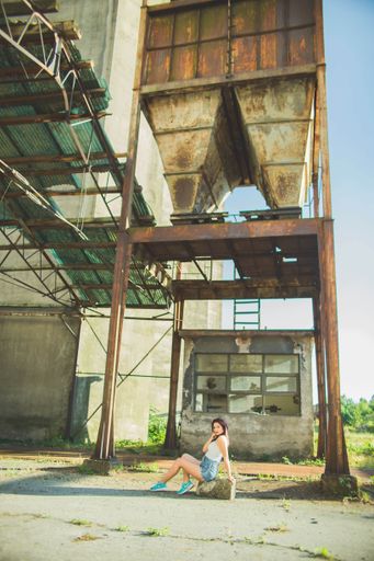 A vertical shot of a cute Caucasian girl sitting on a rock in front of an old building, posing