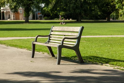 A closeup of a wooden bench  along a concrete path in a park in Rotterdam, The Netherlands