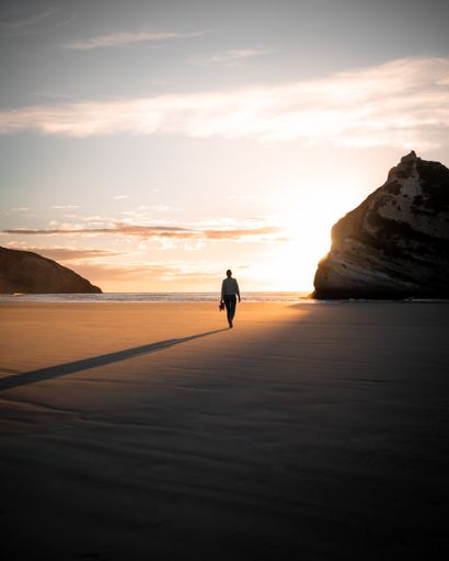 A vertical shot of a person walking on the beach surrounded by the sea and cliffs during the sunrise