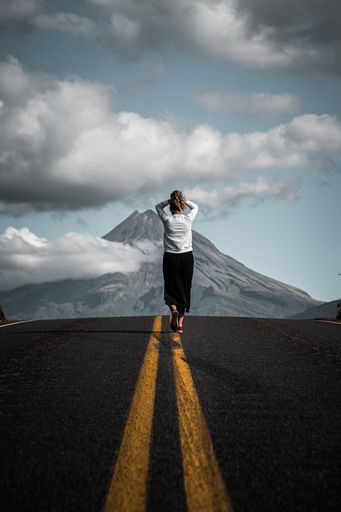 A mesmerizing view of a young tourist walking on the empty road leading to the mountain