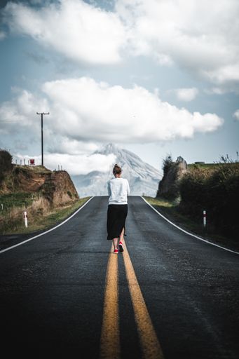 A mesmerizing view of a young tourist walking on the empty road leading to the mountain
