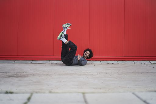A happy young Spanish guy laying on the ground with legs up in the red wall background