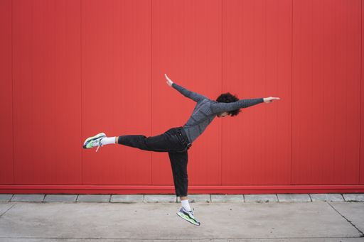A young male in the air; a hip-hop dancer dancing contemporary street dance in the red wall background