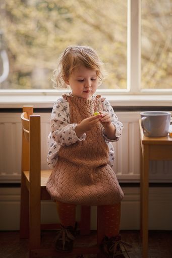 A vertical shot of a little Dutch girl sitting on the chair and holdin a green olive