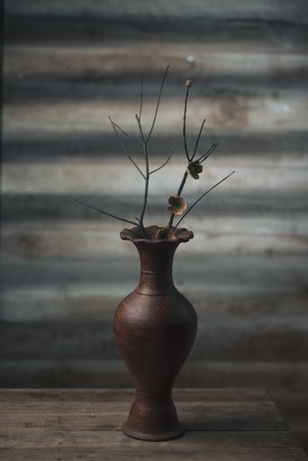 The dry branches with flowers in an antique vase on a wooden table
