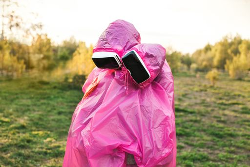 A closeup shot of two people hugging each other in pink plastic raincoats and VR headsets