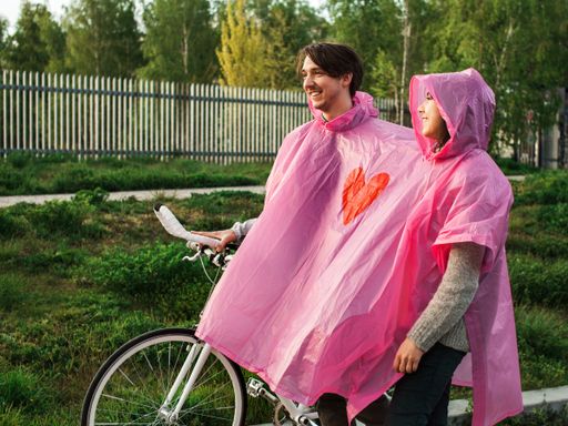 A male and a female in a shared pink plastic raincoat walking with a bicycle on a date
