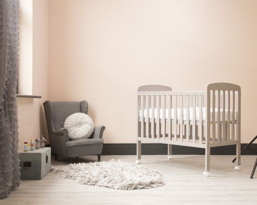 A shot of minimalistic sunny baby's room interior with child's bed, small fluffy carpet, and elegant chair.