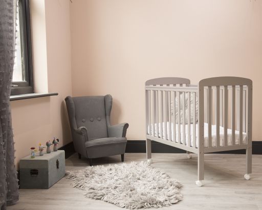 A shot of minimalistic sunny baby's room interior with child's bed, small fluffy carpet, and elegant chair.