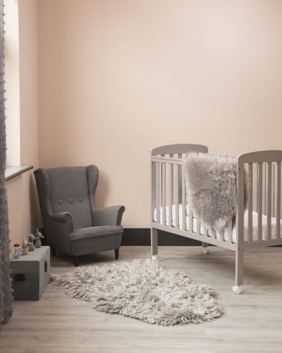 A vertical shot of minimalistic sunny baby's room interior with child's bed, small fluffy carpet, and elegant chair.