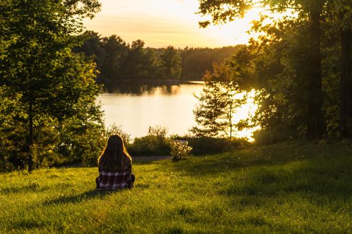 A female sitting on the grassy field enjoying the view with sea and trees in the background
