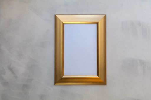 A minimalistic shot of a golden frame for pictures hanging on the indoor wall.