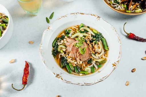 A closeup of delicious noodle soup with greens and sliced roasted meat in a bowl