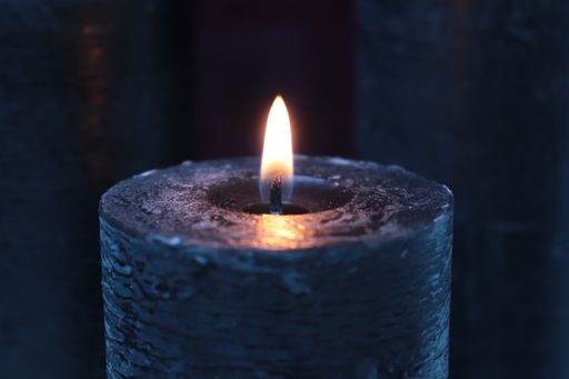 A selective focus shot of a dark-colored burning candle