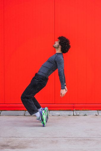 A vertical shot of a Caucasian young athlete posing in front of a red wall
