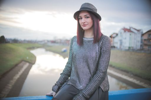 A shallow focus shot of a beautiful Caucasian woman sitting in front of a lake