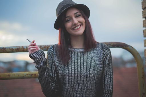 A portrait of a young dark-haired Caucasian female in a hat, smoking in the sunset