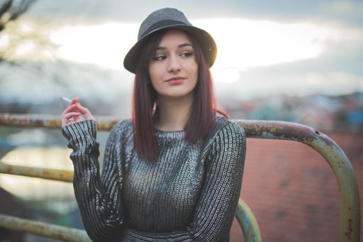 A portrait of a young dark-haired Caucasian female in a hat, smoking in the sunset