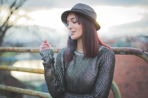 An attractive Caucasian female in a hat smoking cigarette and posing for the camera