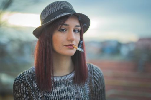 An attractive Caucasian female in a hat smoking cigarette and posing for the camera