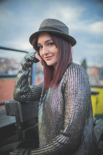 A vertical shot of a Caucasian woman wearing a hat and posing outsid