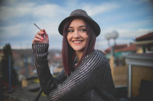 A portrait of a young dark-haired Caucasian female in a hat, smoking in the sunset