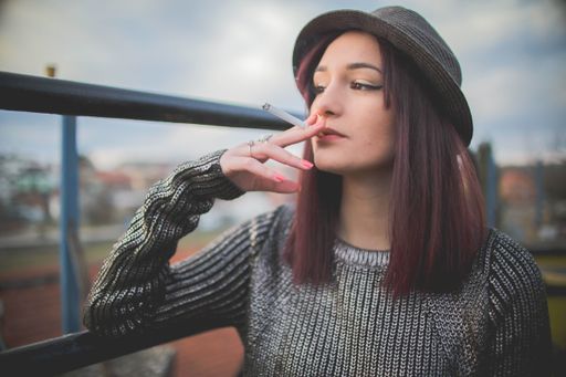 An attractive Caucasian female in a hat smoking cigarette and posing for the camera