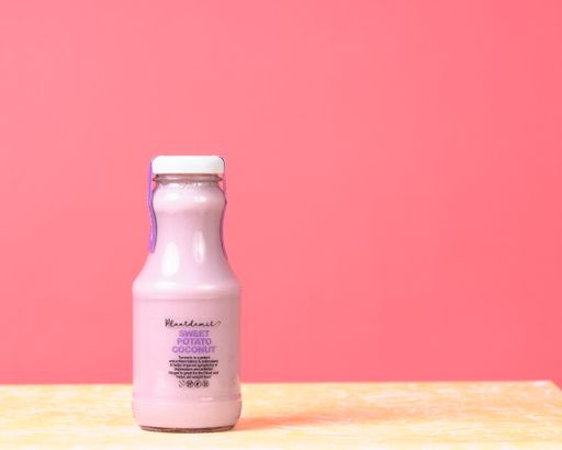 A closeup shot of coconut vegan milk  in a glass bottle on the pink background
