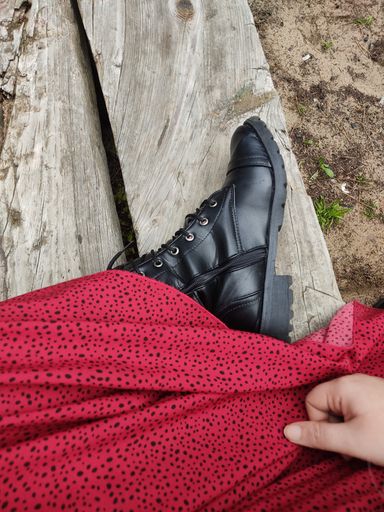 A vertical top view of a woman wearing black boots and a red skirt, sitting on a bench at the beach