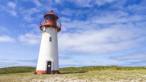 A lighthouse in a meadow under the blue cloudy sky